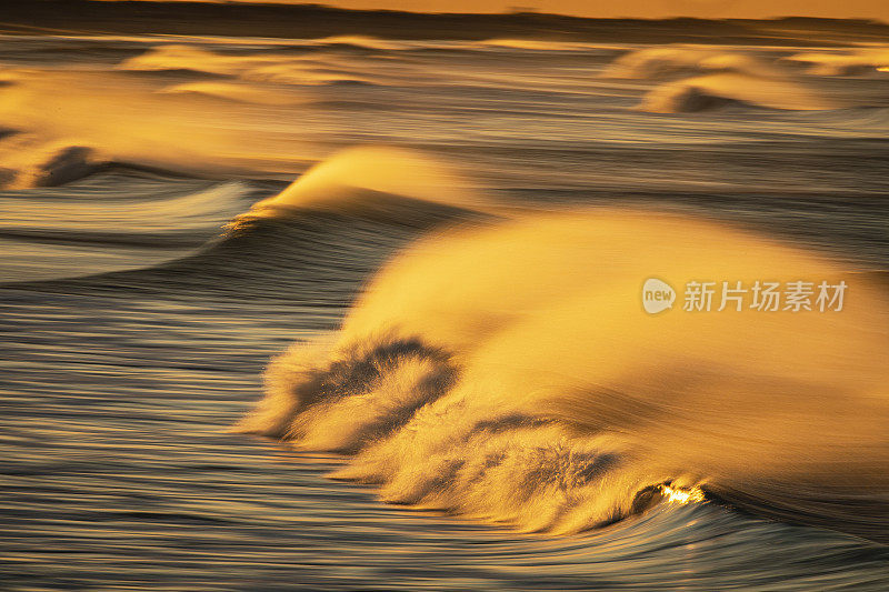 海浪的海景，强风浪花反射出海滩上明亮的金色日出