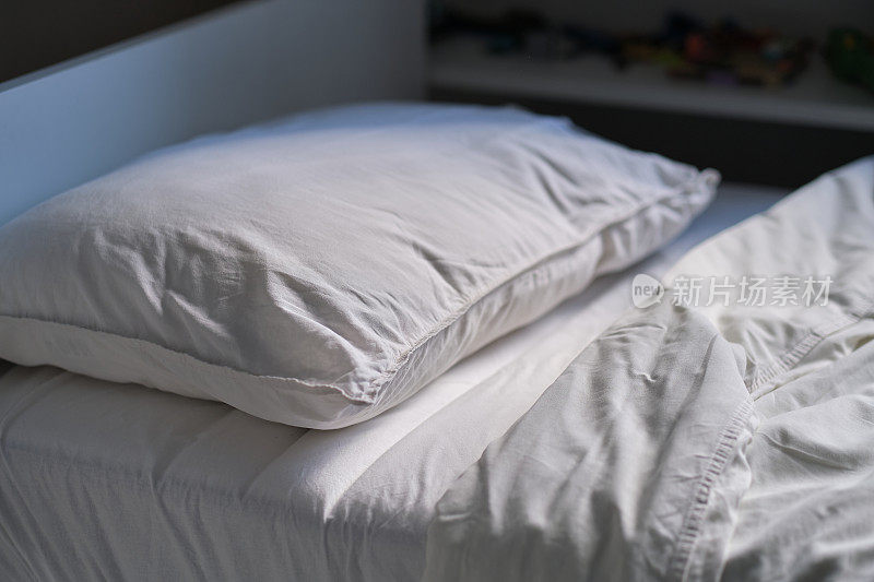 孩子们未整理的床，白色亚麻布，侧视图。柔软的枕头和温暖的毯子