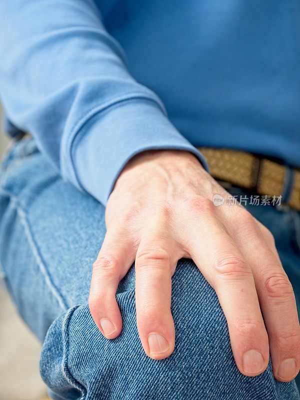 中年白人男子，手放在膝盖上，蓝色色调的衣服