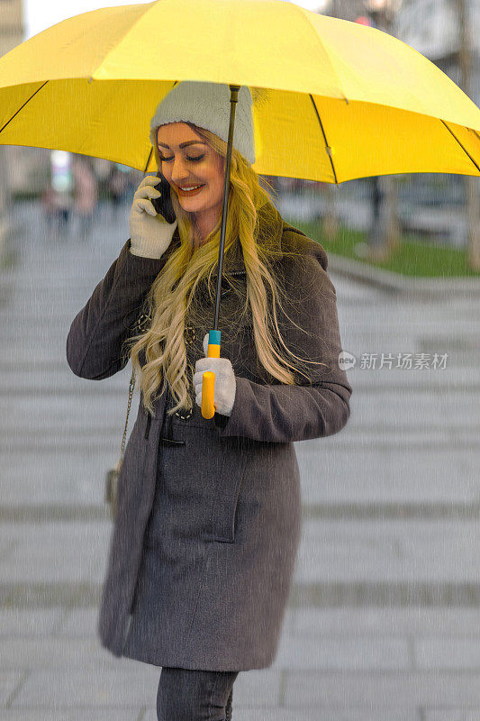 一个迷人的年轻女子在雨天走在城市街道上使用手机的肖像。