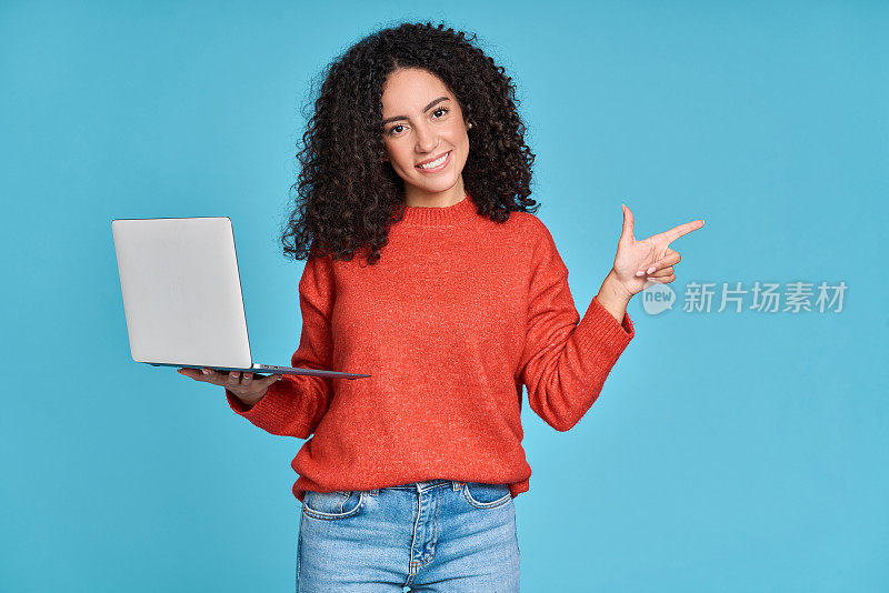 年轻快乐的拉丁女人拿着笔记本电脑指着一边孤立的蓝色。
