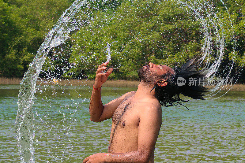 特写:印度男子站在平静的泻湖中，拨弄潮湿的头发溅起水花;热带岛屿天堂;林地与棕榈树的景色;侧影;聚焦于前景