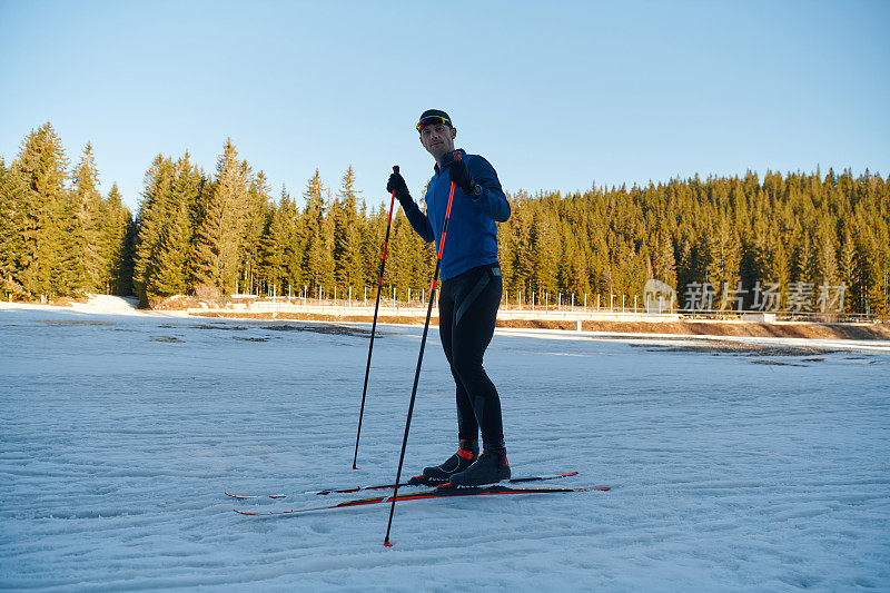 帅气的男性运动员与越野滑雪板准备装备训练在雪林。检查smartwatch。健康的冬季生活方式。