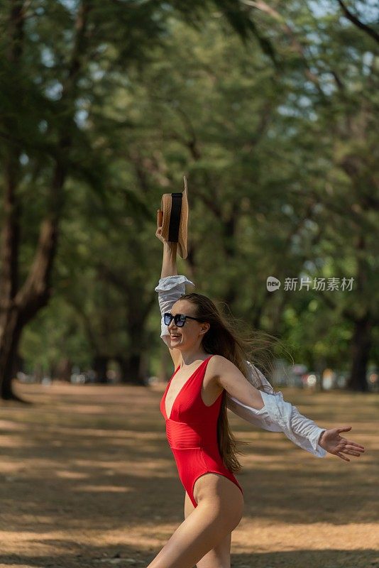 美丽的白人女性性感的女人在红色泳装比基尼寒冷和放松的帽子在她的头上快乐地微笑在森林的海滩