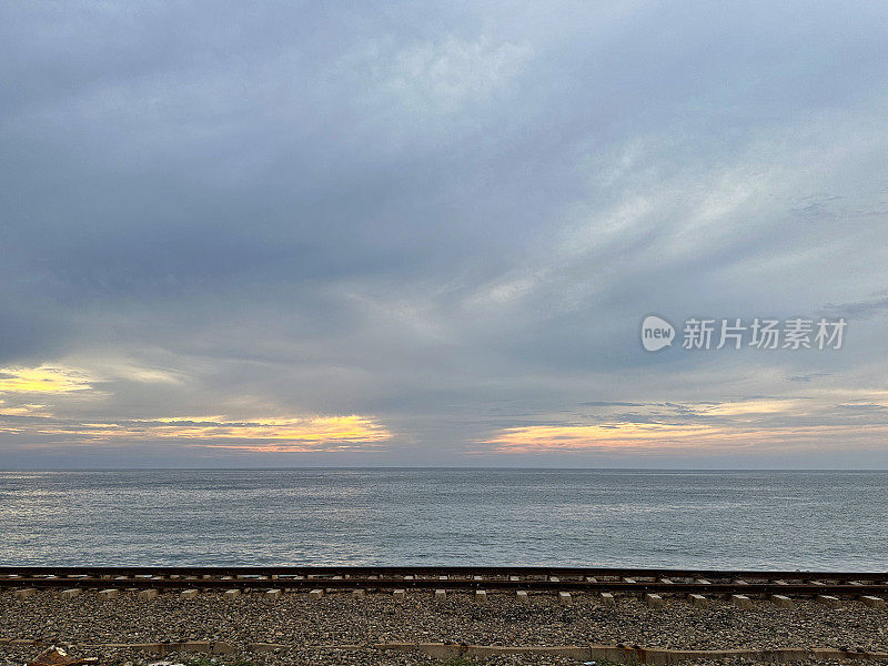 海上的日落天空，空旷的海岸线(南线)铁路线与海岸线平行，金属铁轨和砾石，斯里兰卡科伦坡，前景为焦点