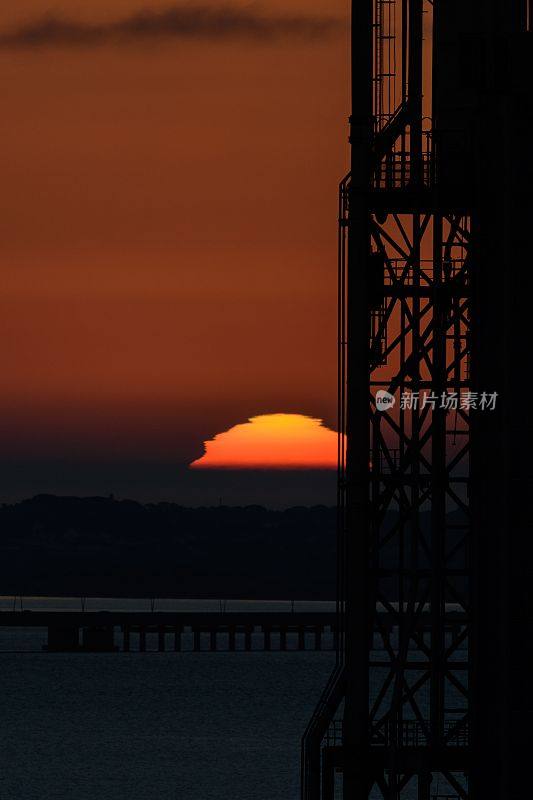 在葡萄牙里斯本，日出在地平线上，穿过一座工业塔。