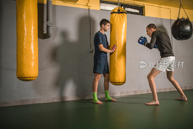 一个强壮的自由搏击运动员在健身房通过踢他的朋友拿着的沙袋进行训练
