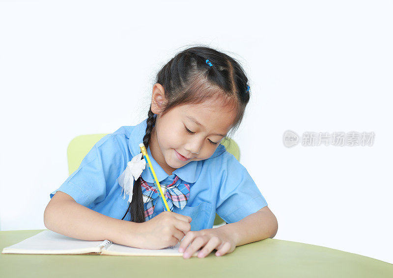 快乐的小女生在白底的书桌上写着笔记本。儿童与教育理念。
