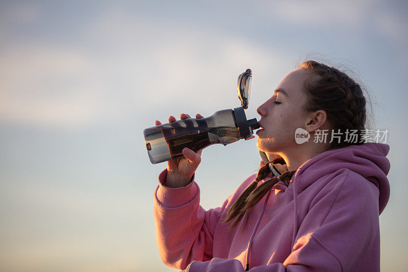 日落时分，年轻的女运动员正在喝水。