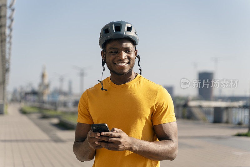 在城市街道上，戴着安全帽拿着手机微笑的积极的非洲男子的肖像