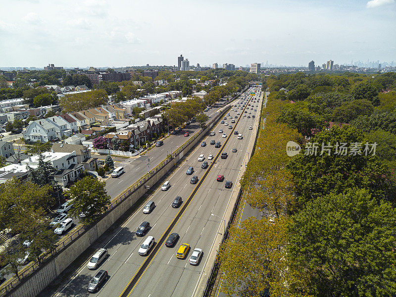 大中央公园路上忙碌的早晨。高速公路交通与纽约皇后区住宅区的城市景观和摩天大楼相映衬，远处的曼哈顿天际线在地平线上。天线的角度来看