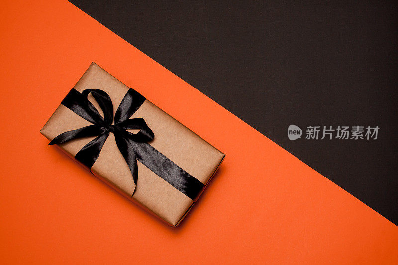 一个用牛皮纸包装的长方形礼品盒，装饰着黑色缎带和蝴蝶结，放在橙黑色的背景上。出售。“黑色星期五”。Flatlay