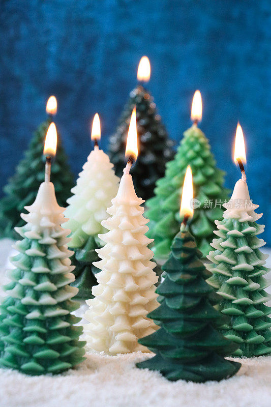 圣诞冷杉森林场景的特写图像，一组点燃的圣诞树蜡烛在人造雪上，斑驳的蓝色背景，重点在前景