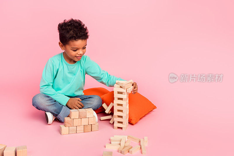 可爱小男孩的全身照片玩叠叠积木游戏穿着时髦的海蓝宝石衣服孤立在粉红色的背景