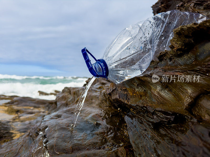 在葡萄牙，一个装满垃圾的空塑料瓶被粗心地遗忘在海滩上的一块岩石上，海水正在释放