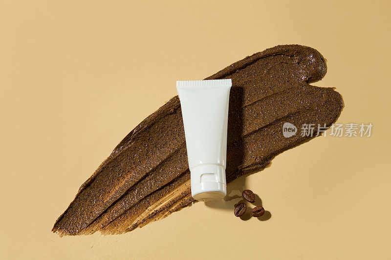 这是一款深棕色的去角质霜，由有机咖啡成分制成，浅棕色背景，顶部有一个白色的空白标签化妆品管，用咖啡豆装饰