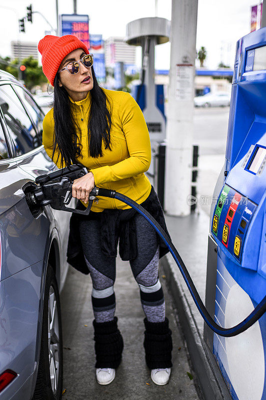 一位现代时尚的女士在加油站给她的车加油，眼睛扫视着加油站的显示