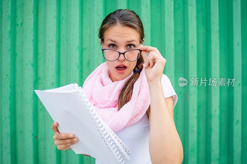 迷人的年轻教师看着她的眼镜拿着笔记本对绿色背景-股票照片
