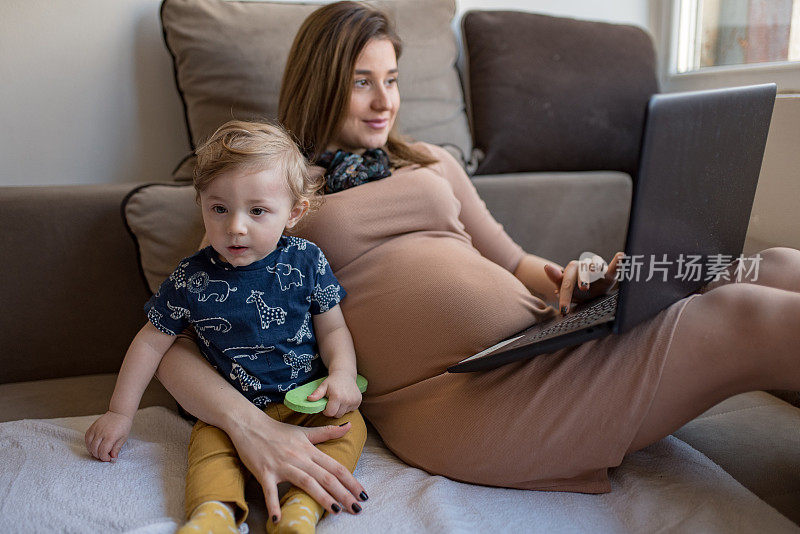 孕妇使用笔记本电脑，照顾她的小儿子