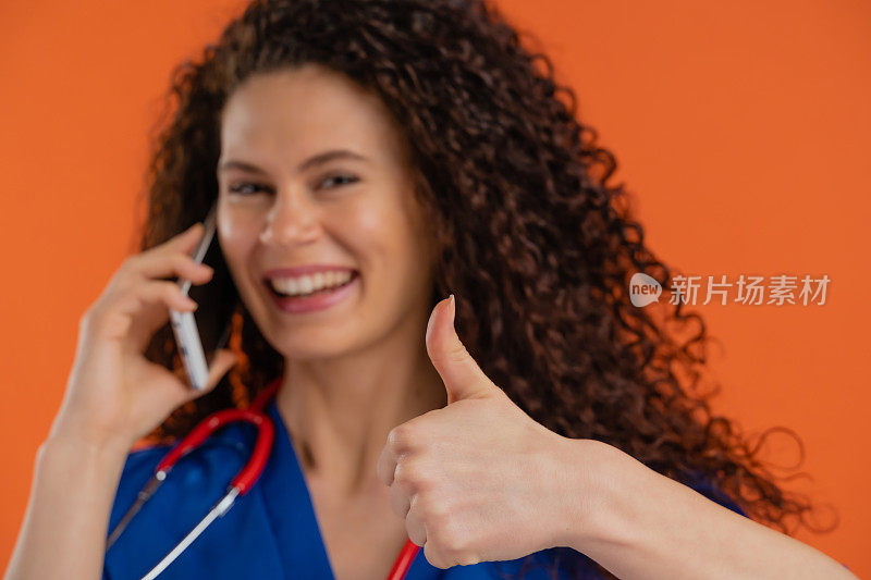 年轻女医生使用智能手机，竖起大拇指，橙色背景