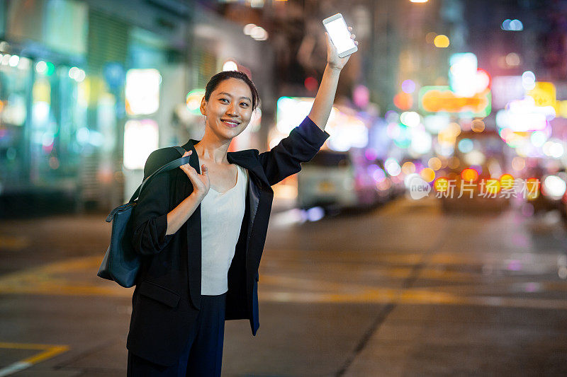 年轻的中国女商人在香港晚上拿着手机叫出租车