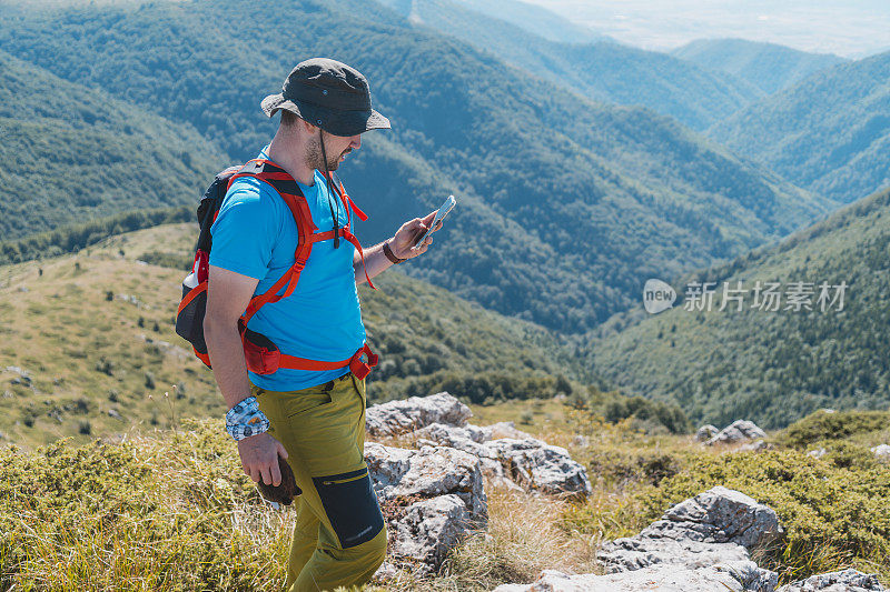 年轻男子在青山边徒步旅行时查看智能手机上的GPS