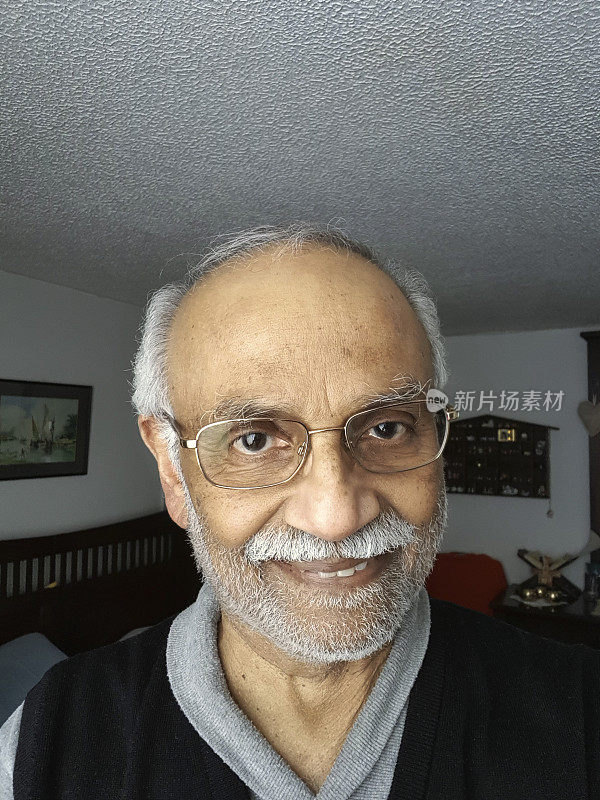 一位72岁微笑的亚洲印度男子在自然光下用手机自拍，他刚刚做完胆囊手术8天;不剃须的笑脸。