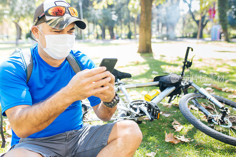 一名男子戴着防护面具坐在草地上用智能手机