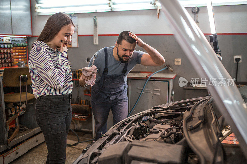 发愁的汽车修理工在汽车修理店向女顾客展示发动机