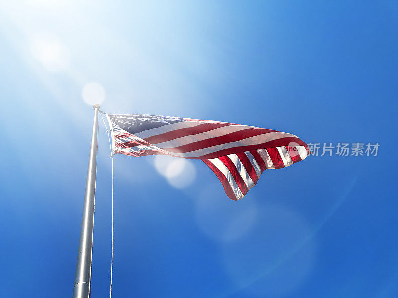 在晴朗的蓝天上，在高高的旗杆上挥舞着美国国旗