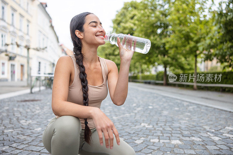 在市中心从塑料瓶里喝水的美丽女人