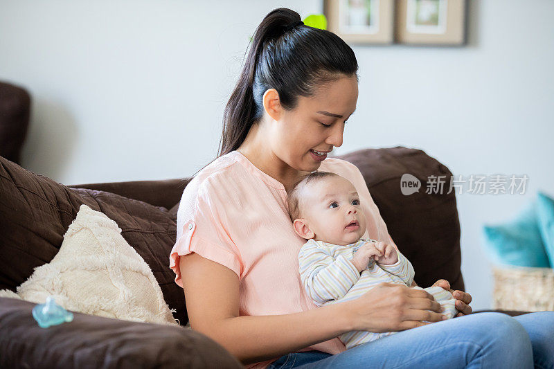 妈妈抱着刚出生的婴儿坐在家里的沙发上