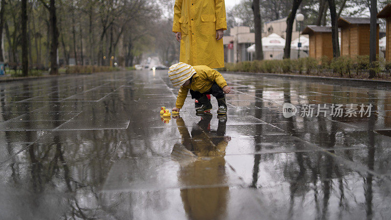 母亲和蹒跚学步的孩子，男孩，在雨中玩耍，穿着靴子和雨衣