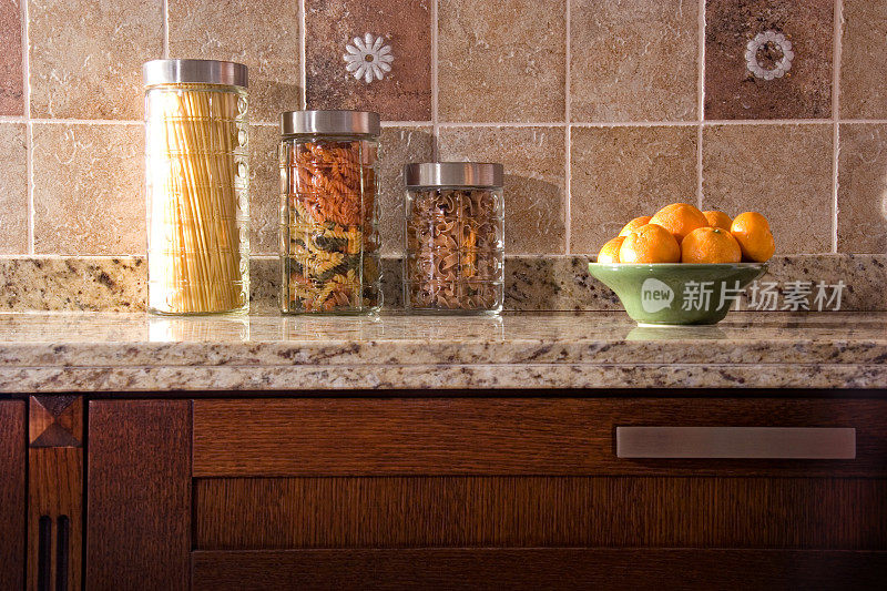 各种各样的意大利面在玻璃罐和橘子在陶瓷碗在家庭厨房柜台
