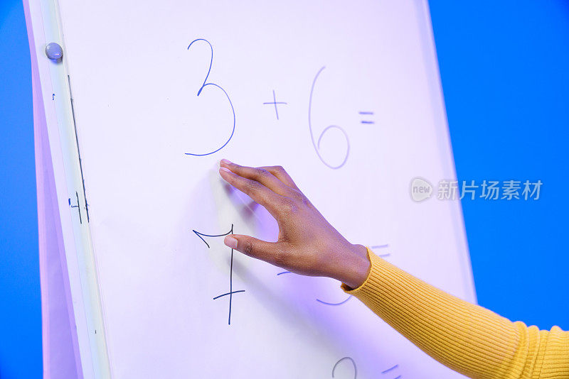 一个深色皮肤的老师的手的特写，在白板上展示数学例子