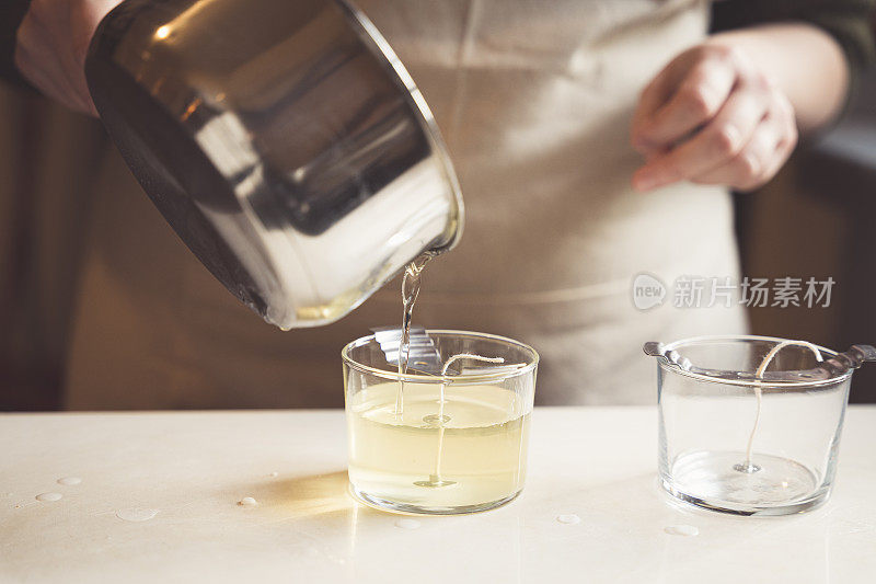 一位妇女将融化的蜡倒入玻璃杯中制作蜡烛