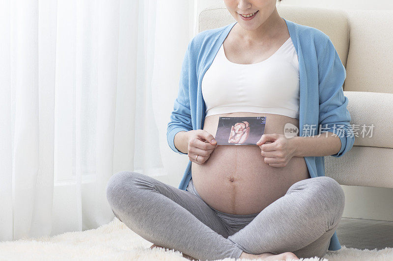 孕妇拿着超音波影像盘腿坐在地上微笑