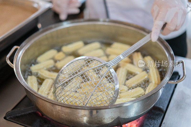 将油条面团倒入炉子上沸腾的油中烹饪