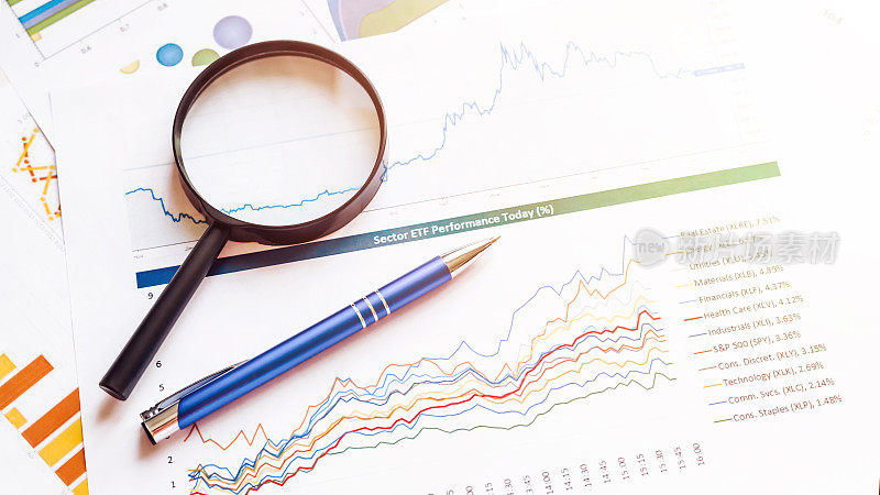 用放大镜和笔在纸上画财务图表。商业会计文件和财务营销图表。