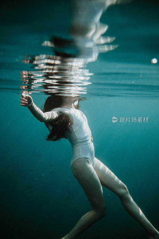 女人长着棕色的头发和白色的泳衣在海里游泳，从水下看