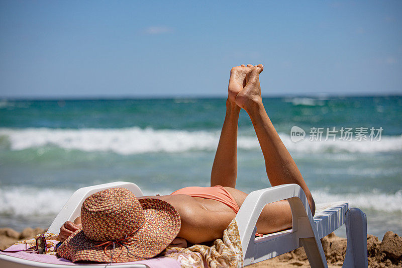 难以辨认的斜躺的女人与白色的帽子在海滩日光浴的背景下的大海，特写