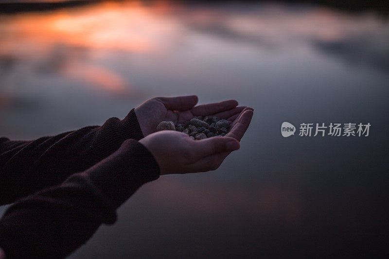 特写女人的手拿着鹅卵石，而站在湖岸