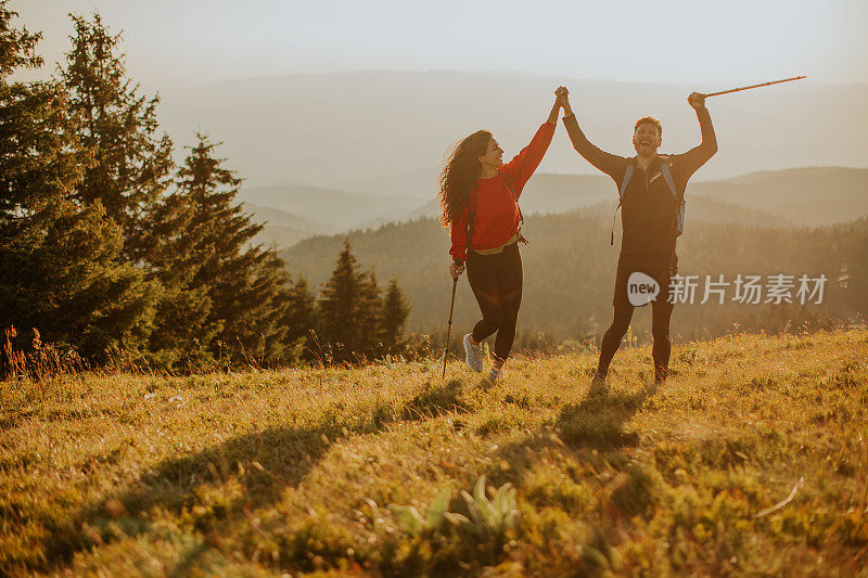 微笑的夫妇背着双肩包走在绿色的山丘上