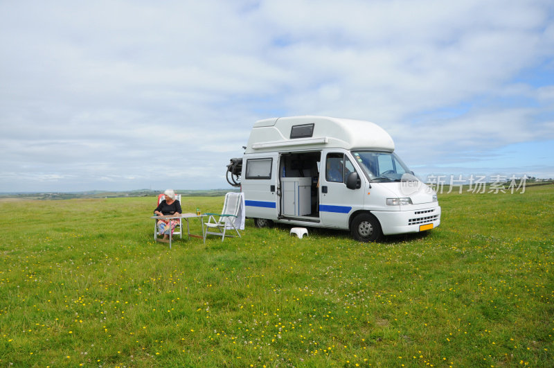 露营车和一个坐在英国草地上的老女人。