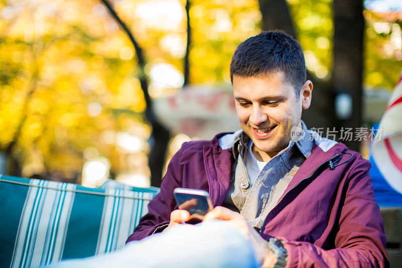 一名男子在户外咖啡厅享用咖啡。使用智能手机。
