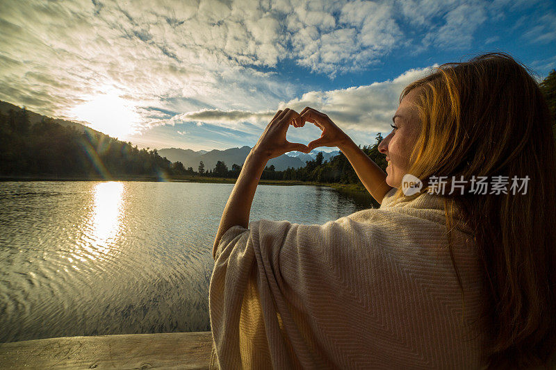 女性在山湖景观上做心形指架