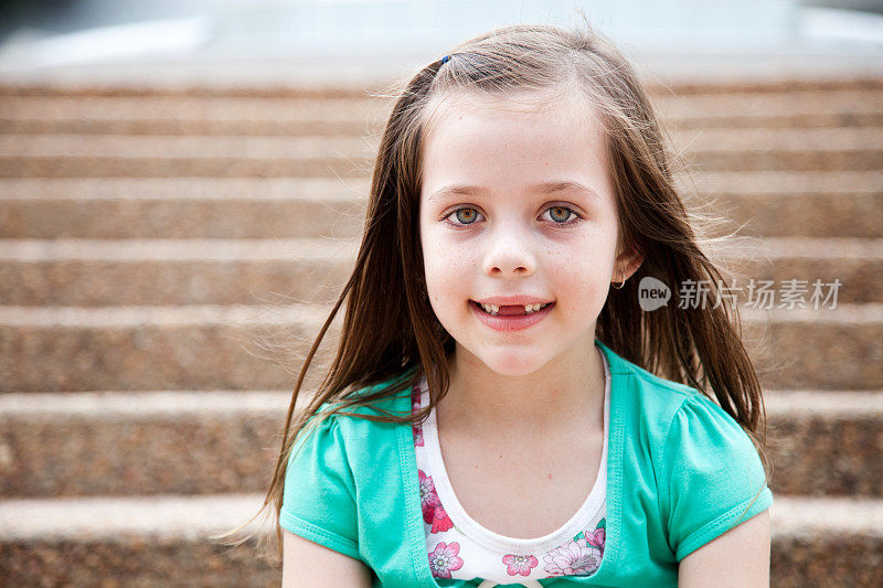 一个棕色长发的白人小女孩坐在户外的楼梯上