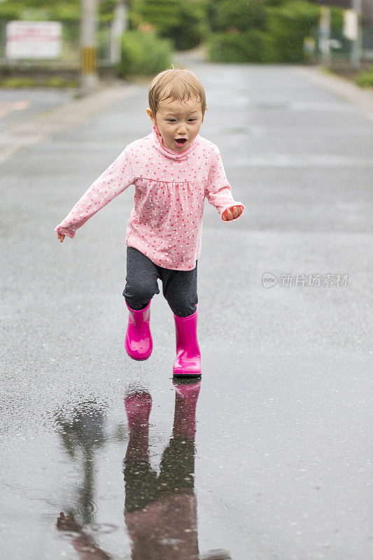 穿着雨靴的小女孩正要跑过水坑