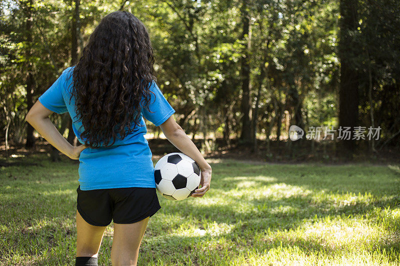 一个十几岁的女孩放学后在户外踢足球。