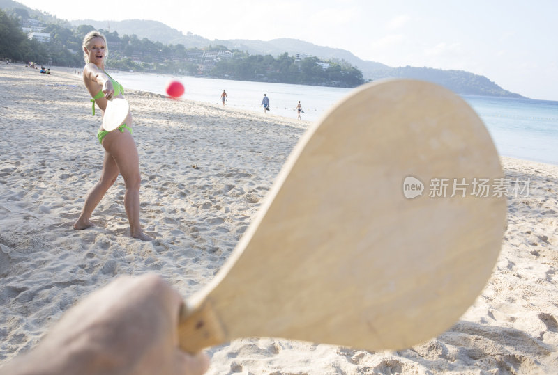 成熟的女人在沙滩上玩平板球